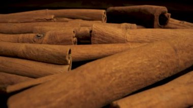 Yakın çekimde bir yığın tarçın çubuğu gösteriliyor. Çubuklar üst üste istiflenmiş, zengin kahverengi renklerini ve desenli yüzeylerini sergiliyorlar..