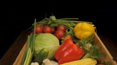 Taze sebzelerle dolu tahta bir sandık. Sandıkta domates, yeşil biber, sarı biber, lahana, salatalık, soğan ve mısır gibi çeşitli renkli ürünler bulunuyor..