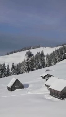 Huzurlu bir dağ manzarasında, karla kaplı çam ağaçları ve rahat kulübelerin sergilendiği sakin bir manzara. Dikey görüntüler