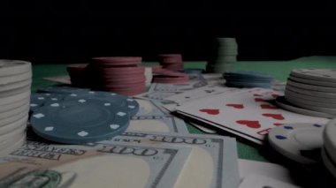 Yüzeyine saçılmış poker fişleri, kartlar ve paralarla dolu yeşil bir keçeli masa resmi. Çipler farklı renklerde ve nakit para Amerikan doları..