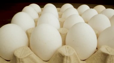 Karton bir karton kutuda beyaz tavuk yumurtası yakın çekim. Yumurtalar sıra sıra dizilir ve karton kahverengi kartondan yapılır. Video, karanlık bir stüdyoda çekiliyor..