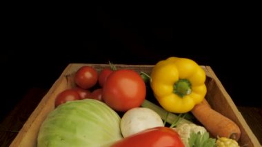 Bir ahşap kutu çeşitli taze sebzelerle dolup taşıyor, renkli ve çeşitli ürünler sergileniyor. Sarı ve kırmızı dolma biber ve mısır bir kutuya konur..