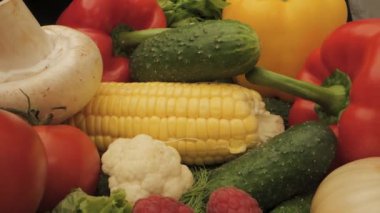Canlı renklerini ve dokularını gözler önüne seren taze sebze ve mısırın yakın plan görüntüsü. Çeşit çeşit kırmızı dolma biber, yeşil salatalık, beyaz mantar ve sarı mısır kulağı içerir.