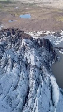 Uçsuz bucaksız bir buzulun, engebeli uçurumlarla çevrili derin mavi çatlakları. Güneş ışığı İzlanda 'daki Svinafellsjokull Buzulu' nun zıt dokularını vurgular. dikey görüntüler