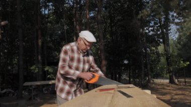 Tecrübeli bir zanaatkar, odunu dikkatlice testereyle biçerek, huzurlu bir ormanın benekli güneş ışığı altında, işçiliğin ruhunu somutlaştırarak, güzel bir eser haline getirir..