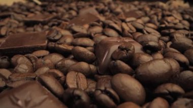 Kavrulmuş kahve çekirdekleri arasına saçılmış koyu çikolata parçalarının yakın çekim görüntüsü. Görüntü, her iki bileşenin de zengin kahverengi renklerine ve dokularına odaklanır..