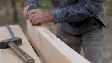 Bir zanaatkârın yakın çekimi, sakin bir ormanda bir el uçağıyla ahşap kirişi ustalıkla şekillendirir. Sahne, marangozluk ve doğayla olan bağlantıyı vurguluyor..