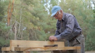 Tecrübeli bir zanaatkar eski bir uçağı kullanarak tahtayı dikkatlice inceler. Etrafı uzun ağaçlar ve doğal ışıklarla çevrili, işine odaklanıyor ve ağır işçilikten zevk alıyor..