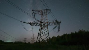 Gece vakti yüksek voltajlı elektrik kablolarının gece vakti görünümü ay ışığında hareket eden yıldızların arkaplanına karşı. Elektrik ve enerji üretimi kavramı