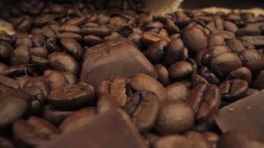 Kavrulmuş kahve çekirdekleri arasına saçılmış koyu çikolata parçalarının yakın çekim görüntüsü. Görüntü, her iki bileşenin de zengin kahverengi renklerine ve dokularına odaklanır..
