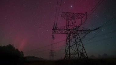 Güzel aurora ışıkları gece gökyüzünde dans ediyor, sakin bir kırsal alanda elektrik hatlarını aydınlatıyor. Çarpıcı görüntü nefes kesici bir atmosfer yaratıyor..