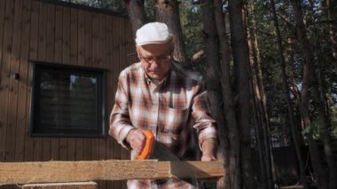 Kıdemli bir zanaatkar, güneşli bir öğleden sonra güneşi altında yemyeşil ağaçlarla çevriliyken dikkatle odun kesmeye odaklanır. Doğanın sakinliği anı güçlendirir..