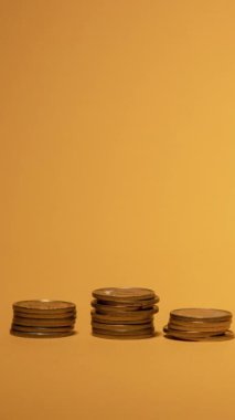 Birkaç madeni para yığını, finansal büyüme ve yatırımı sembolize eden canlı sarı bir zemin üzerinde yükselen bir sıraya göre düzenli olarak düzenlenmiştir. Düzenleme, zenginliğin farklı seviyelerini vurguluyor.