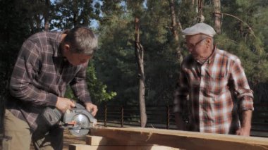 İki yetenekli zanaatkar, yüksek ağaçların arasında bir marangozluk projesinde işbirliği yapıyor. Onlar dikkatle odunları kesmeye odaklanırken güneş parlıyor..