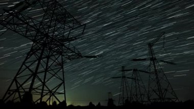 Yıldızların büyüleyici hareketine tanık olun. Karanlık bir gökyüzüne karşı izler oluşturan, yüksek elektrik hatlarının üzerine kurulmuş. Sakin atmosfer bu göksel görüntünün güzelliğini arttırıyor..