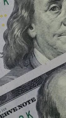 Görüntü, Benjamin Franklin 'in yüz dolarlık banknotlardaki portresini detaylı bir şekilde gösteriyor, banknotun karmaşık desenlerini ve dokusunu vurguluyor,.