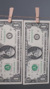 Bir dolarlık banknotlar ahşap mandallarla bir çamaşır ipine bağlanıyor, farklı tasarımlarını sergilerken gri bir zemine asılılar. dikey görüntüler
