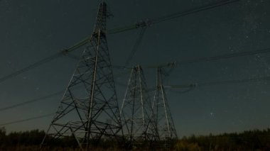 Gece vakti yüksek voltajlı elektrik kablolarının gece vakti görünümü ay ışığında hareket eden yıldızların arkaplanına karşı. Elektrik ve enerji üretimi kavramı. Zaman aşımı