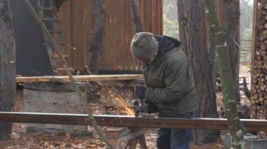 Elektrikli alet kullanan bir adam, soğuk havada ağaçlar ve açık hava malzemeleriyle çevrili bir ormanda metal projesinde çalışırken kıvılcımlar yaratıyor..