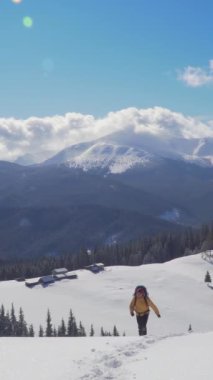 A solitary hiker is climbing a snowy trail, surrounded by majestic mountains and a clear blue sky. The vibrant landscape emphasizes the beauty of winter in the mountains. Vertical footage