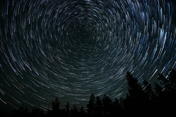Yıldızlar karanlık bir ormanın üzerinde gece gökyüzünde güzel izler bırakırlar. Dünya 'nın dönüşünü sergilerken aynı zamanda dingin manzarayı aydınlatırlar..