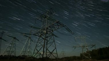 Geceleyin uzak bir arazide yüksek enerji hatlarının üzerinde dönen yıldız izlerini yakalar, teknoloji ve doğa arasındaki zıtlığı vurgular..