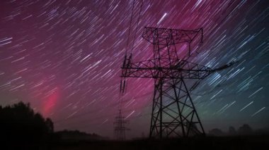 Uzun pozlama, yıldızların ritmik dansını ve yukarıdaki auroraları yakalar sakin kırsal bir alanda, çarpıcı bir gece gökyüzü altında canlı renklerle dolu..