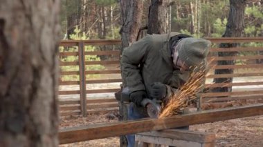 Sıcak giysili ve bereli biri açık havada metal bir parça üzerinde çalışıyor. Kıvılcımlar uçar, tıpkı bir öğütücü gibi sakin bir ormanda metali şekillendirirler..