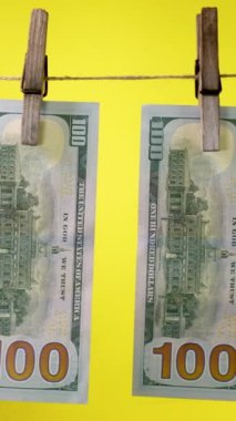 Sarı arka planda çamaşır iğnesi ipinde dolar kurur. Dolar 'ın finansal konsepti. İpte 100 dolarlık banknot. Para aklama konsepti. Dikey görüntüler