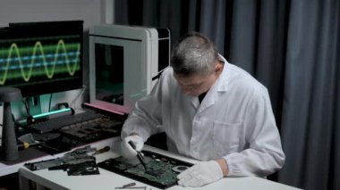 Beyaz laboratuvar önlüklü bir teknisyen, elektronik sinyaller gösteren hassas aletler kullanarak bir devre kartında özenle çalışır..
