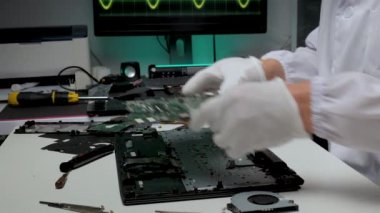 Eldiven giyen bir teknisyen, temiz ve yüksek teknolojili bir laboratuarda karmaşık devre kartları üzerinde dikkatle çalışır. Çalışma alanı etrafında araçlar ve ekipmanlar düzenlenir.
