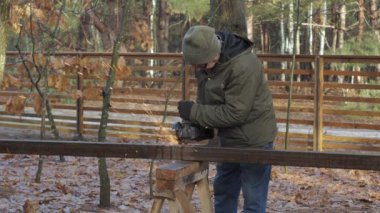 Bir zanaatkar ağaçlık alanda öğütücüyle metal kesmeye odaklanır. Maddeyi şekillendirirken kıvılcımlar uçuşuyor, doğadaki sanatına bağlılığını gösteriyor..