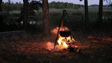 Kavurucu bir kamp ateşinin üzerine asılmış bir tencere alacakaranlık çöktüğünde bölgeyi aydınlatıyor. Sakin göl sönen ışığı yansıtır, barışçıl bir atmosfer yaratır..