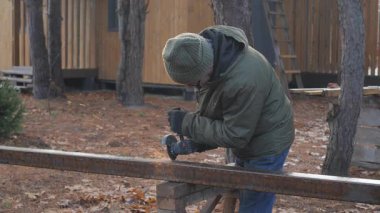 Ormanlık alanda el bilgisayarı kullanan bir insan metali kesiyor. Ağaçlar ve kırsal binalarla çevrili temiz gökyüzünün altında görevlerine odaklanırken kıvılcımlar uçuşuyor..