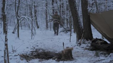 Karlı bir ormanda şöminenin yanında sıcak bir geceye hazırlanan bir adam toplanır. Yakınlarda bir çadır ve kamp ateşi görülebilir..
