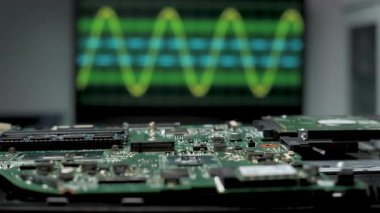Arka planda bir osiloskop dalgalı elektronik sinyalleri gösterirken bir devre kartı ön plana yerleştirilir. Burası modern bir laboratuvar..