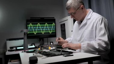Yetenekli bir teknisyen düzenli bir tezgahta elektronik aletleri tamir etmeye odaklanır. Araçlar ve ekipmanlar düzenlenmiştir ve arka planda dalga formlarını gösteren bir monitör vardır..