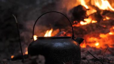 Kırsal bir siyah çaydanlık, parlayan közlerle çevrili açık bir ateşin üzerinde ısınır. Vahşi doğada mükemmel bir hayatta kalma ve çalılık sahnesi..