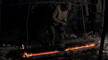 Bir adam, gece yarısı, bir far ile aydınlatılmış, ormanın derme çatma bir barınağının altında, parlayan bir kamp ateşinin yanında oturur. Sahne, hayatta kalmanın vahşi ruhunu yakalıyor..