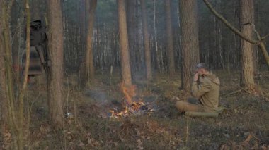 Ormanda kamp ateşinin yanında oturan adam Bushcraft Survival 'da çalışıyor, çam ormanında tek başına ısınan kampçı, barışçıl orman yaşamının tadını çıkarıyor.