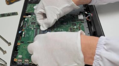 Bir teknisyen, bir dizüstü bilgisayarın ana kartının parçalarını dikkatlice yerleştirirken düzenli, iyi aydınlatılmış bir çalışma alanında koruyucu eldivenler takıyor..