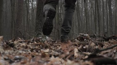 Yapraklarla kaplı ormanda yürüyen adam, sonbaharın sonlarında sisli ve soğuk bir ormanda düşen yapraklara basan botların yakın çekimi..