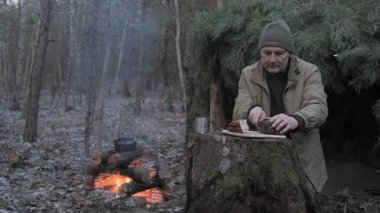 Orman kampında kırsal yemek hazırlayan adam, ateş, duman ve basit açık hava yemek hazırlama sahnesi.