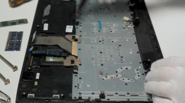 Teknisyen, temiz bir atölye ortamında eldiven takan bir dizüstü bilgisayarı dikkatlice manipüle ederek tamir sürecine odaklanıyor..