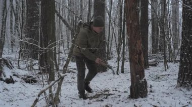 Uzun ağaçlarla çevrili karlı bir ormanda bir adam odun kesiyor. Kar yağışı, o baltayla çalışırken sakin bir kış ortamı yaratır.