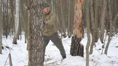 Kış Çalılığı - Ormandaki Ağacı Kesmek - Yeşil bereli ve haki renkli ceketli bir adam karlı bir ormanda bir ağacı kesiyor
