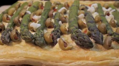 Kuşkonmaz turtası, zeytinli ve peynirli puf böreği, yeşil kuşkonmazlı ev yapımı tart, dilimlenmiş yeşil zeytin, ve çıtır puf börek tabanlı peynir.