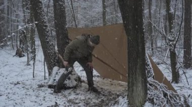 Kar taneleri yağarken, kar ormanlarının birinde geçici bir barınağın yanında oturan bir insan teçhizat hazırlıyor. Sahne, kış kampının sessiz güzelliğini yakalar..