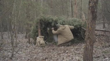 Ormandaki çam dallarından inşa edilmiş kış çalı sanatı barınağı. Sessiz bir ormanda, el yapımı bir çam ağacının altına sığınan bir adam.