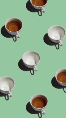 Açık yeşil arka planda bir sürü çay fincanı ve boş fincanı olan desen. Sıcak içecekli çay fincanları farklı yönlere hareket eder. dikey görüntüler